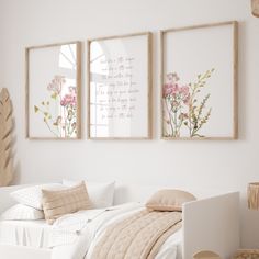 two framed pictures hang above a bed in a white room with pink flowers on the wall