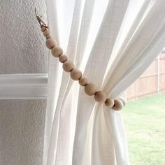 a beaded curtain is hanging in front of a window with white drapes and green grass