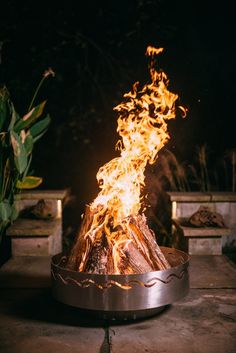 a fire pit sitting on top of a cement floor next to a potted plant