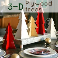 three wooden christmas trees sitting on top of a table next to plates and silverware