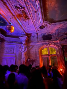 a group of people standing around in front of a building with lights on the ceiling