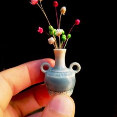 a tiny vase with flowers in it being held by someone