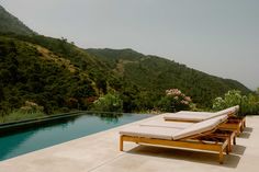 two chaise lounges sitting on the edge of a pool with mountains in the background