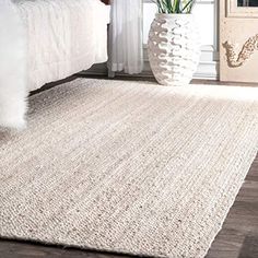 a large white rug in a bedroom next to a bed with a vase on the floor