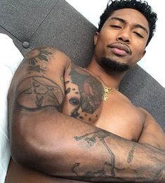 a man with tattoos laying on a bed next to a white pillow and pillows,