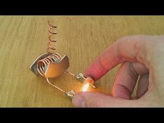 a hand holding a small light bulb on top of a wooden table next to a piece of metal wire