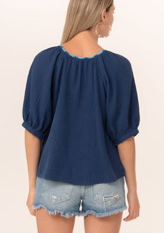 A navy blue bohemian puff sleeve blouse designed in soft cotton gauze. Cotton gauze Relaxed fit Short raglan puff sleeve Round neckline with contrast thread detail Button front Bohemian summer blouse A contrast thread detail adds a unique charm to this classic bohemian blouse. Designed in soft cotton gauze, featuring raglan puff sleeves, a flattering scooped neckline, and a button front. Model is 5'9, wearing a size S.Style: I-15055W-RJZ Bohemian Cotton Peasant Top With Puff Sleeves, Blue Blouse With Gathered Short Sleeves, Blue Summer Top With Elastic Sleeves, Blue Bishop Sleeve Blouse, Spring Cotton Gauze Blouse, Casual Cotton Gauze Short Sleeve Tops, Casual Short Sleeve Cotton Gauze Tops, Blue Blouse With Bishop Blouson Sleeves, Blue Top With Gathered Short Sleeves