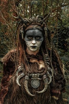 a man with long hair and makeup is dressed up as a horned creature in the woods