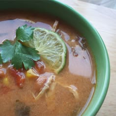 a green bowl filled with soup and garnished with cilantro, limes, and tortilla chips