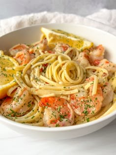 a white bowl filled with pasta, shrimp and lemon wedges on top of a table