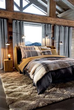 a large bed sitting under a window next to a wooden floor covered in blankets and pillows