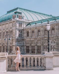 a woman in a white dress is standing on a bridge near a large building with a green roof