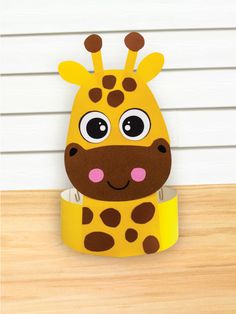 a cardboard giraffe head sitting on top of a wooden table next to a white wall