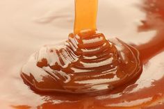 a spoon full of caramel sauce on top of some white and brown liquid in a bowl