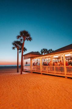 people are sitting at tables on the beach under palm trees in front of an oceanfront restaurant