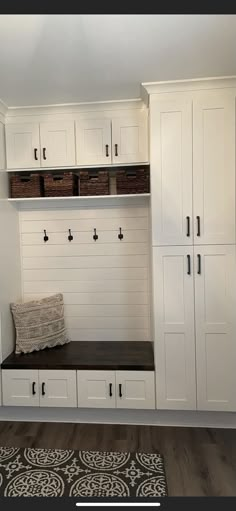 a room with white cabinets and black bench in the center, along with baskets on the wall