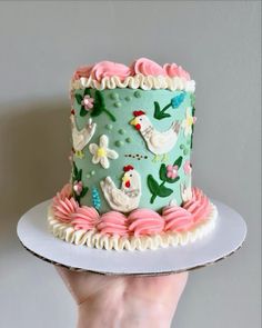 a hand holding a cake decorated with hens and flowers