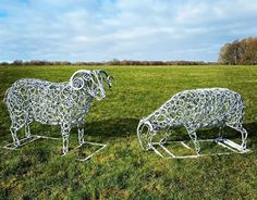 two metal sheep sculptures sitting on top of a lush green field