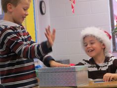 two young boys sitting at a table in front of a present box and one boy wearing a santa hat