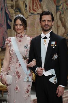 a man and woman standing next to each other in formal wear, wearing tiaras