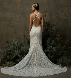 a woman in a white wedding dress standing next to some bushes and trees with her back turned towards the camera