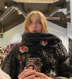 a woman taking a selfie in front of a mirror with her cell phone and scarf around her neck