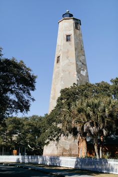 a tall tower with a clock on it's side next to trees and a white picket fence