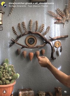 a person pointing at an eye made out of branches and pine cones on a wall