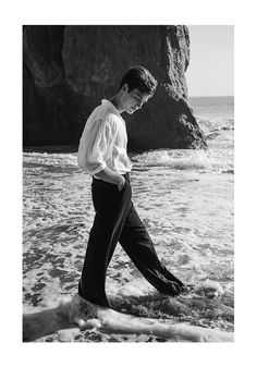 black and white photograph of a man walking in the water at the edge of the ocean