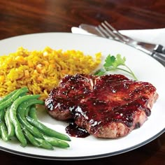 a white plate topped with meat, rice and green beans on top of a wooden table