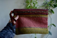 a hand holding a small pouch made out of woven material with a plant in the background