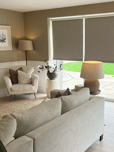 a living room filled with furniture and a large window covered in roman blind shades on the windowsill