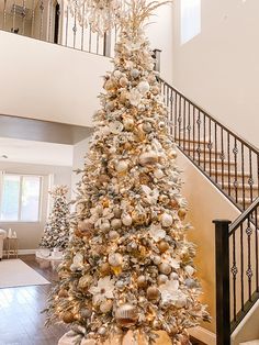 a decorated christmas tree in the middle of a living room with stairs and railings