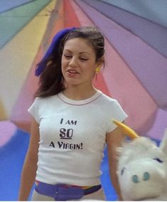 a woman in white shirt walking next to a unicorn toy and rainbow colored umbrellas