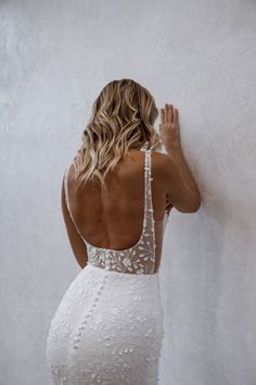 a woman in a white dress leaning against a wall with her back to the camera