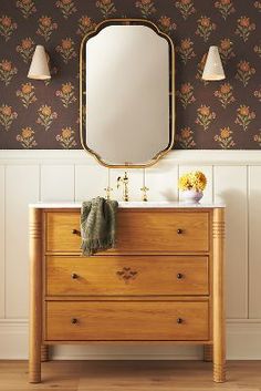 a wooden dresser sitting under a mirror next to a wall with flowers on the walls