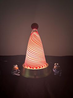 a red and white striped light sitting on top of a metal stand next to two small figurines