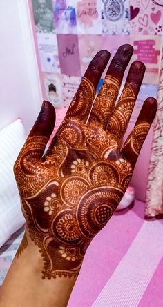 a woman's hand with henna on it and pink bedding in the background