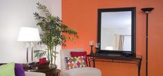 a living room with an orange wall and white chairs in front of a large mirror