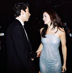 a man in a tuxedo and a woman in a sequin dress smile at each other