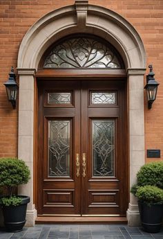 a pair of double doors in front of a brick building with two potted plants