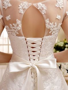 the back of a woman's wedding dress with white flowers and lace on it