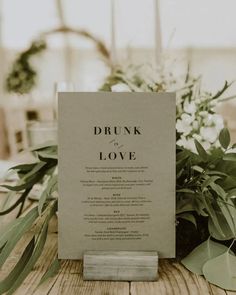 a menu card sitting on top of a wooden table next to flowers and greenery