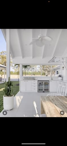 an outdoor kitchen and dining area in a house with white walls, wood floors and ceiling fans