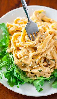 a fork is stuck into some pasta on a white plate with lettuce and parmesan cheese