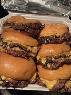 four cheeseburgers in a take out container with aluminum foil