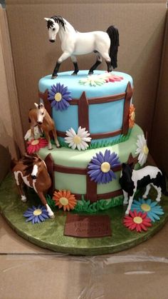 a birthday cake decorated with horses and daisies is in a box on the table