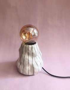 a white and black lamp sitting on top of a pink table next to a light bulb