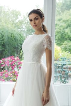 a woman in a white dress standing by a window