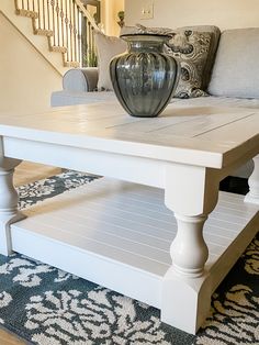 a coffee table with a vase on top of it in front of a stair case